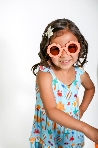 Young girl wearing a colorful dress with a pattern of sea creatures and heart-shaped sunglasses on a white background