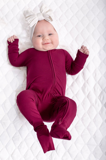 Baby in a maroon onesie with a white bow on a white quilted background