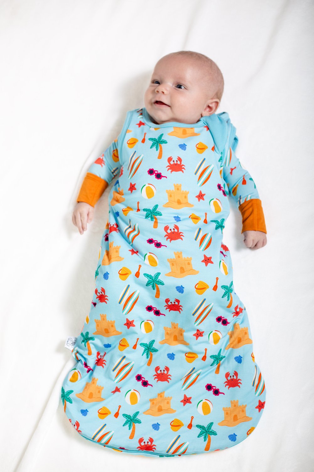 Baby in a colorful sea-themed sleeping bag on a white background