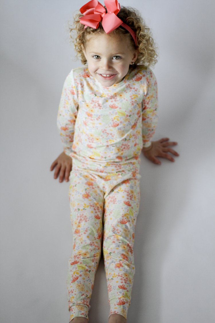 Child wearing a floral outfit with a pink bow on a plain background