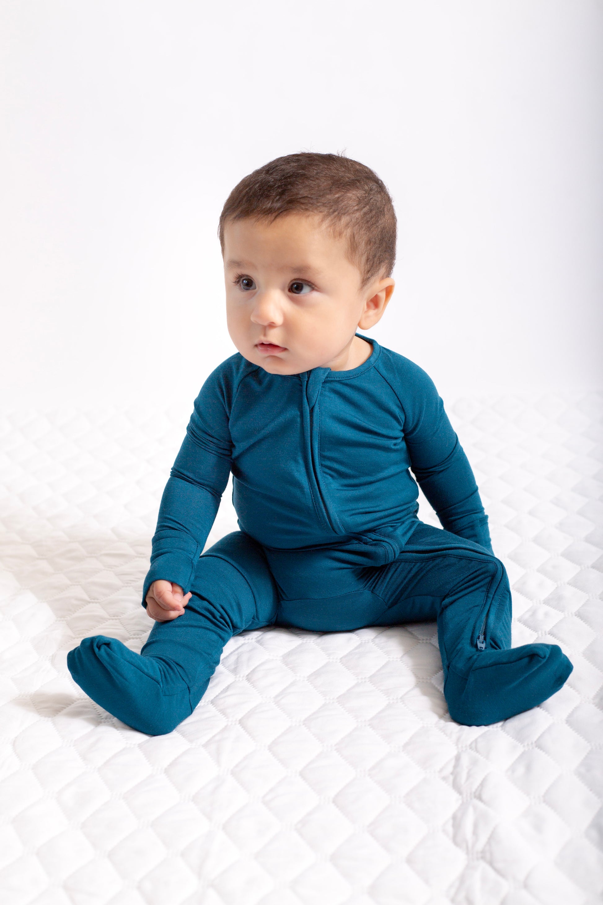 Baby wearing a blue onesie sitting on a white surface