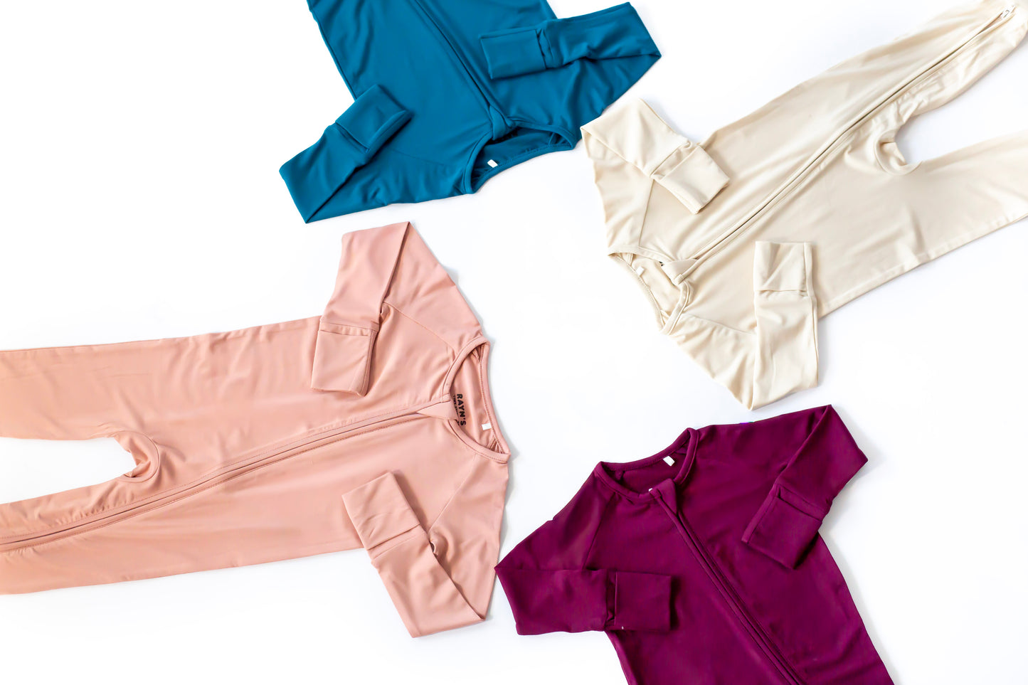 Four pieces of children's clothing in blue, beige, pink, and purple on a white background