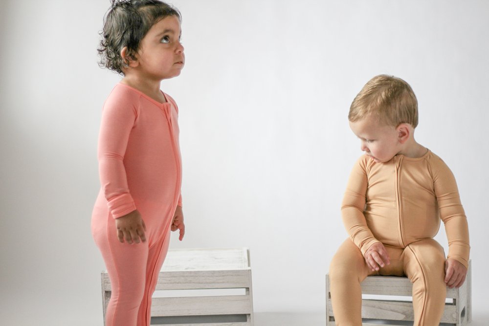 Two children wearing pink and beige onesies on a white background