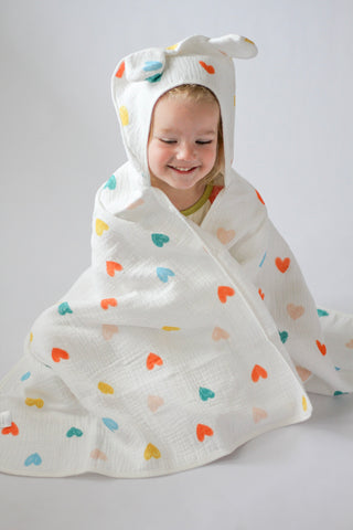 Child wrapped in a colorful heart-patterned hooded towel on a plain background