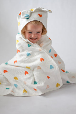 Child wrapped in a colorful heart-patterned towel with a hood on a plain background