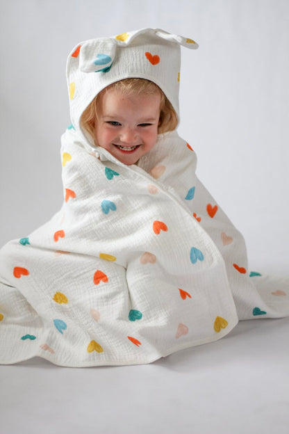 Child wrapped in a colorful heart-patterned towel with a hood on a plain background