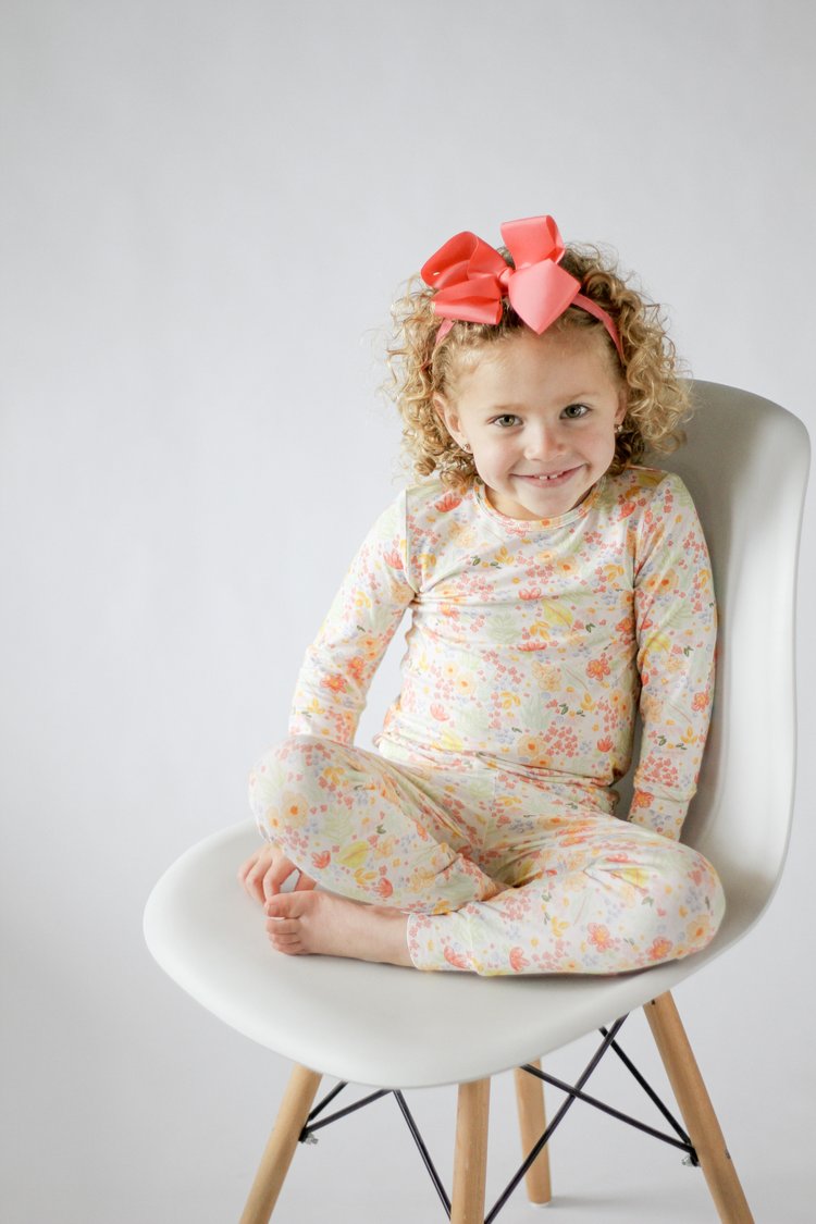 Child wearing a floral outfit sitting on a white chair with a plain background