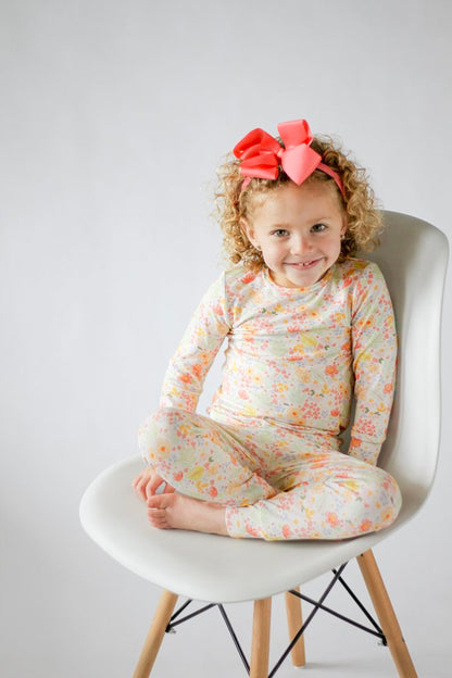 Child wearing a floral outfit sitting on a white chair with a plain background
