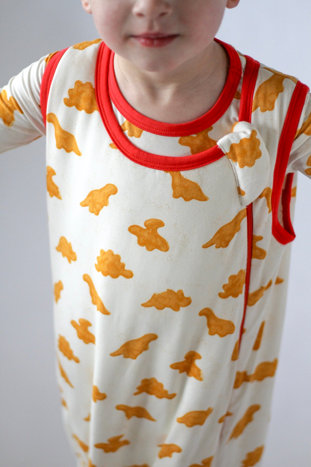 Child wearing a white onesie with orange cloud patterns and red trim.