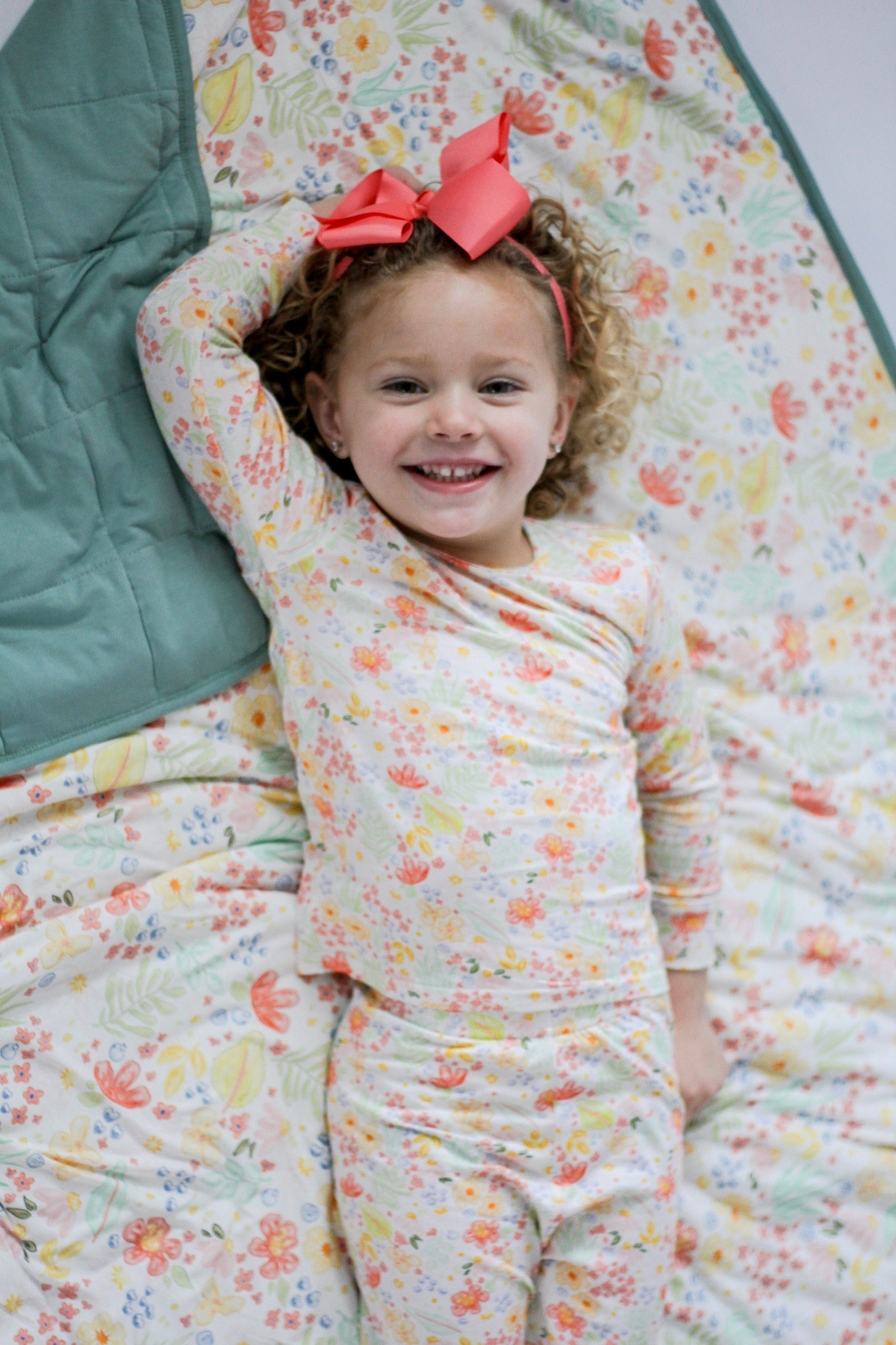 Child wearing a floral outfit and pink bow, lying on a floral blanket