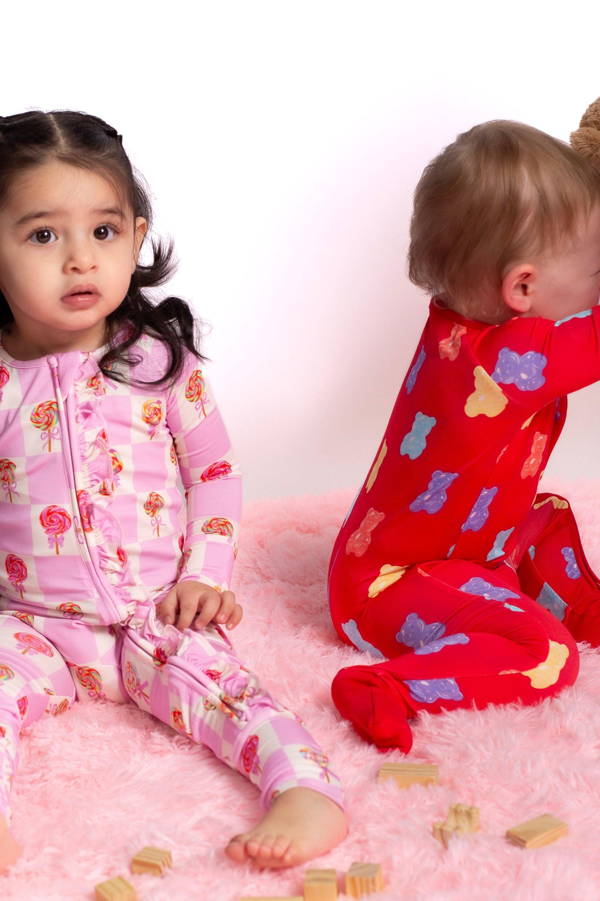 Two children in pajamas sitting on a pink surface with toys around.
