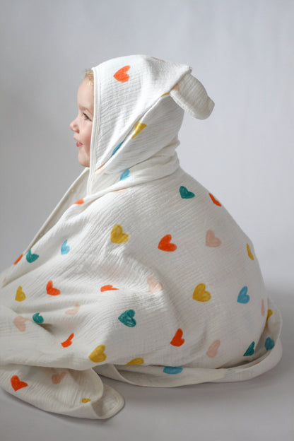 Child wrapped in a white blanket with colorful heart patterns on a plain background