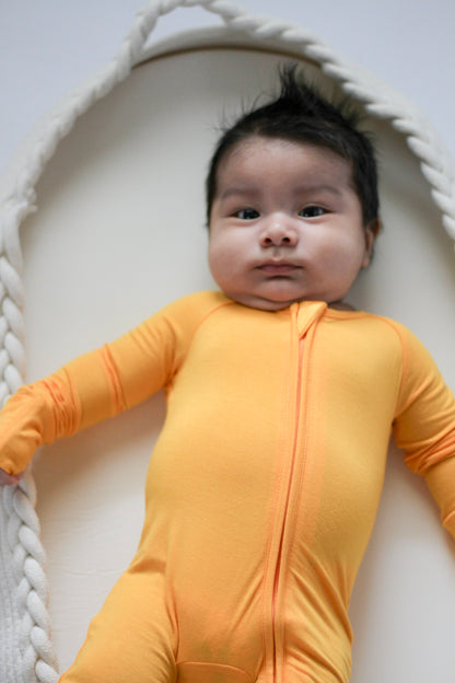 Baby wearing an orange onesie lying on a white surface with a textured white rope border.
