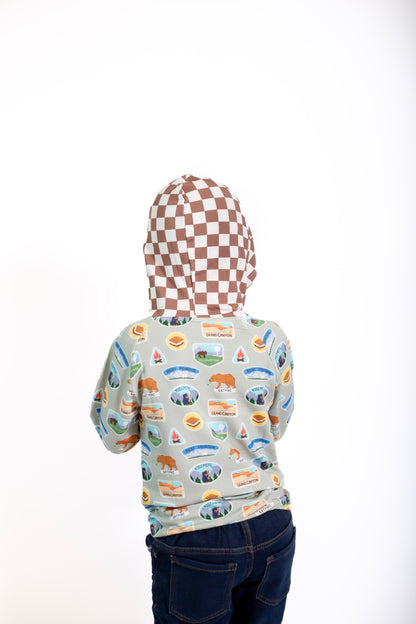 Person wearing a hoodie with a checkered pattern on the back and a colorful patterned shirt on the front, standing against a white background.