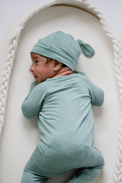 Baby in a light blue outfit and hat lying on a textured white surface