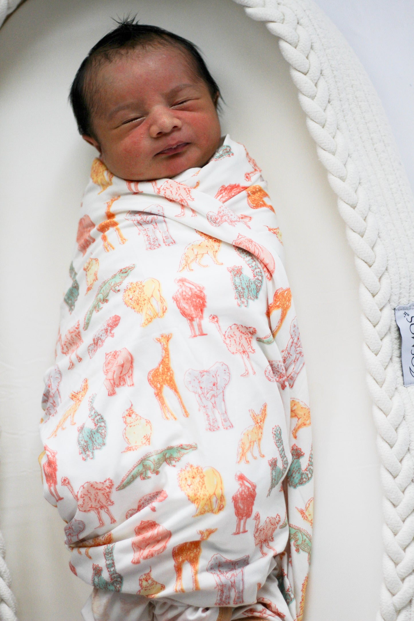 Newborn baby swaddled in a blanket with animal patterns, lying in a white crib.