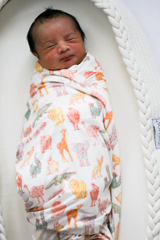 Newborn baby swaddled in a blanket with animal patterns, lying in a white crib.