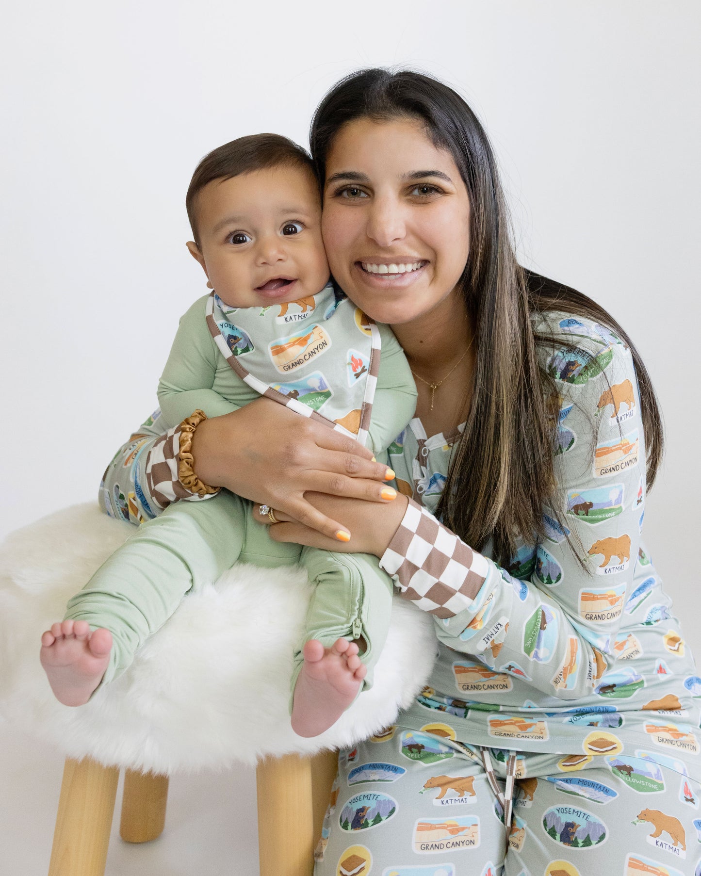 Woman holding a baby both wearing matching pajamas with animal prints on a white background