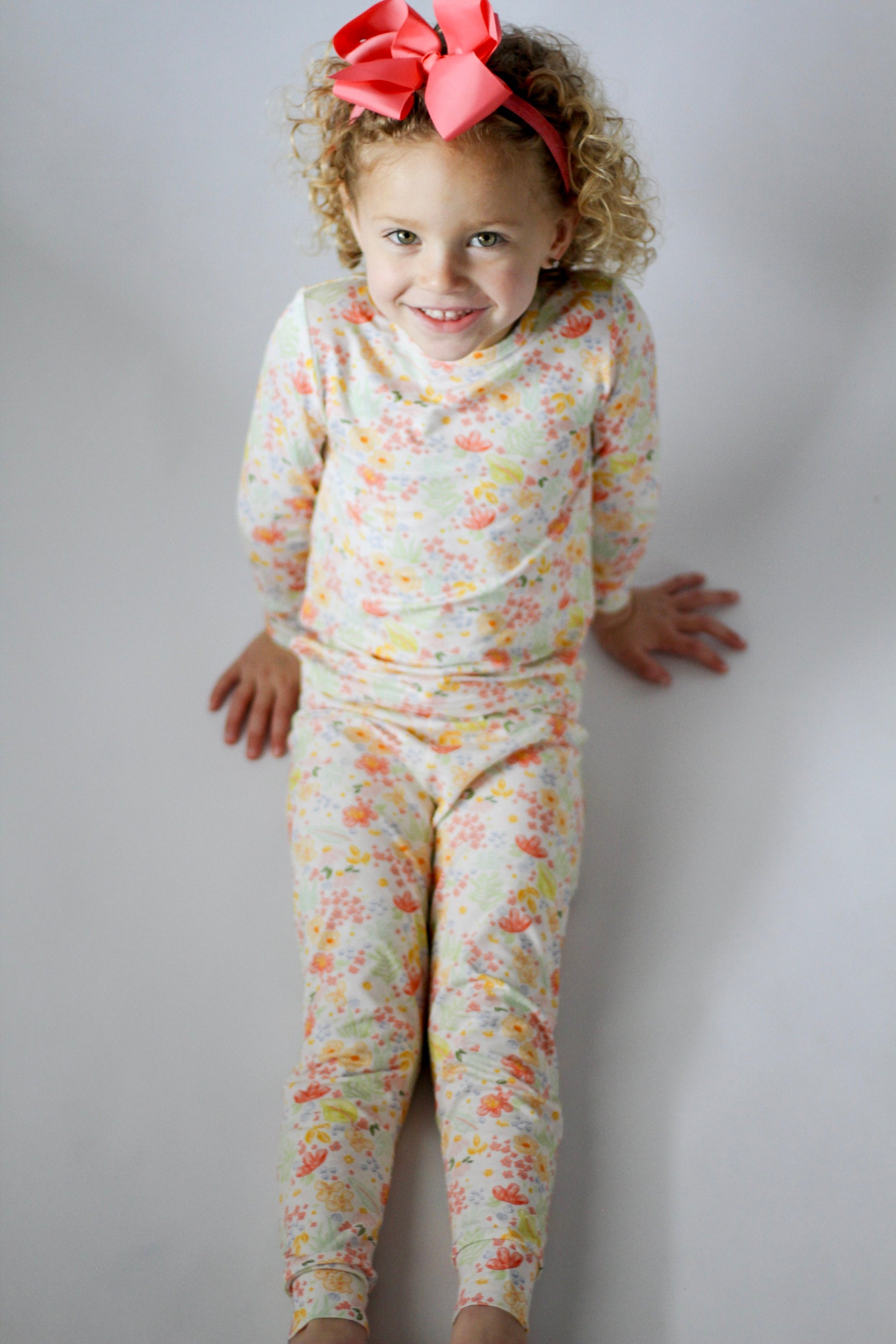 Child wearing a floral outfit with a pink bow on a plain background