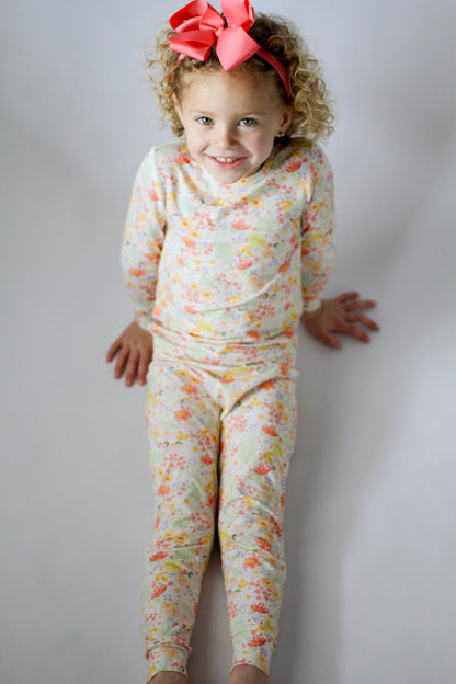 Child wearing a floral outfit with a pink bow on a plain background