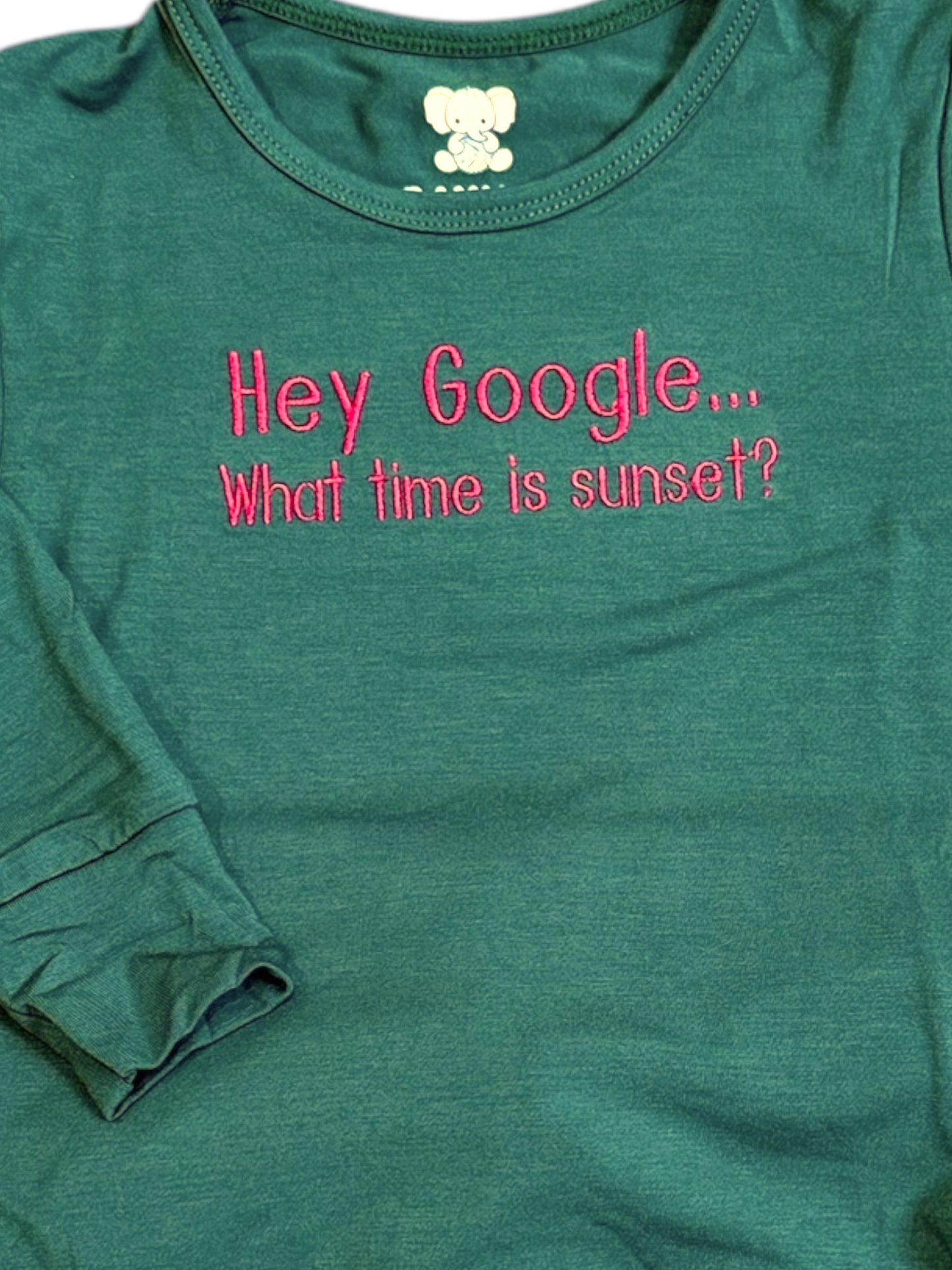 Green t-shirt with pink text 'Hey Google... What time is sunset?' on a white background