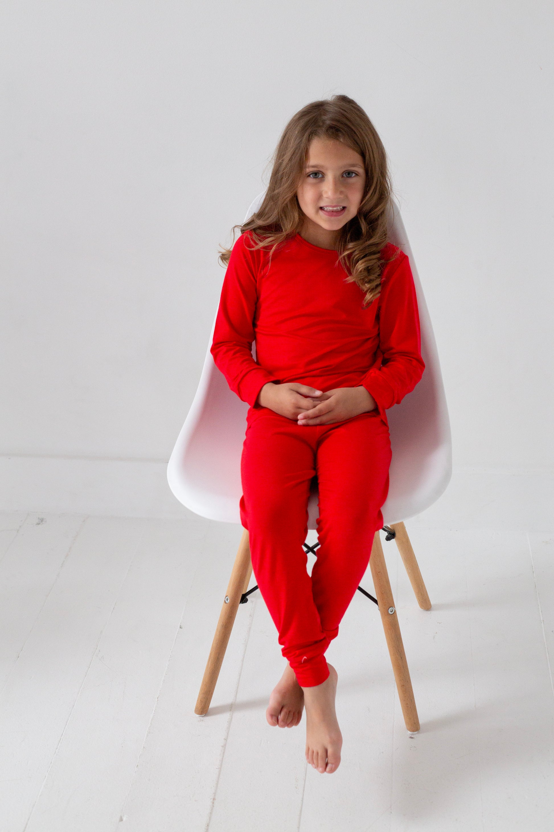 Young girl wearing a red outfit sitting on a white chair against a light gray background