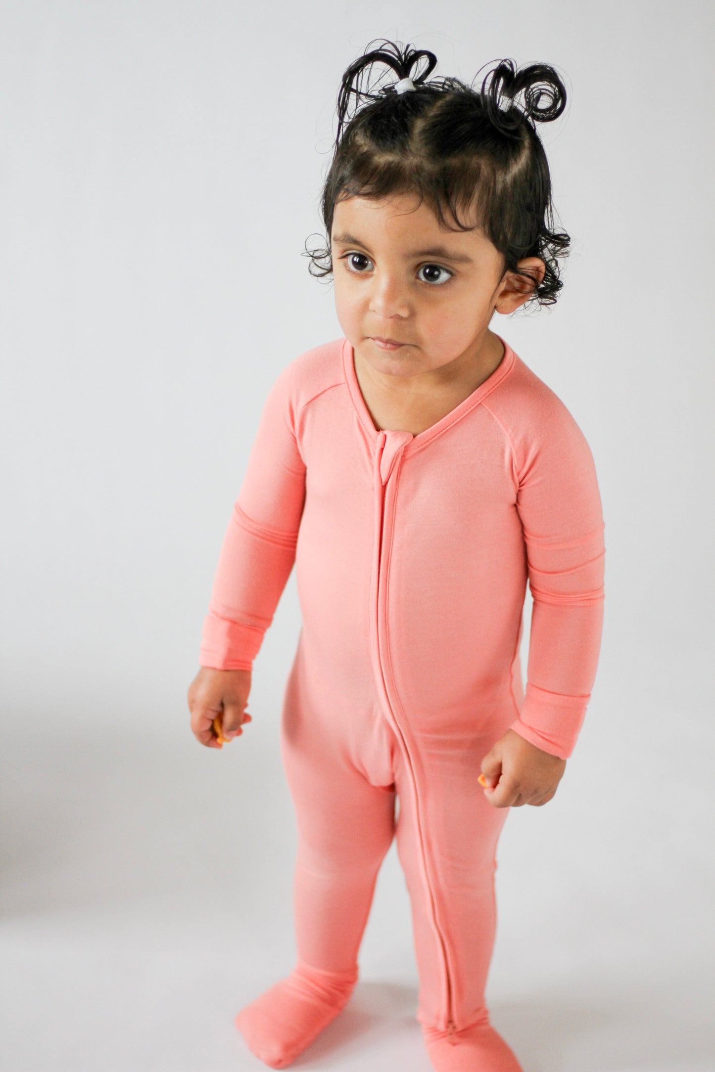 Child wearing a pink onesie against a white background