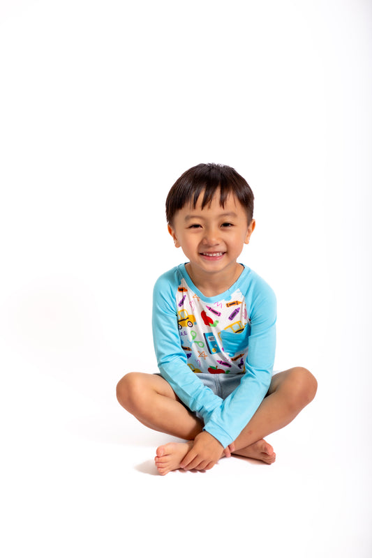Child wearing a light blue shirt with colorful designs sitting on a white background