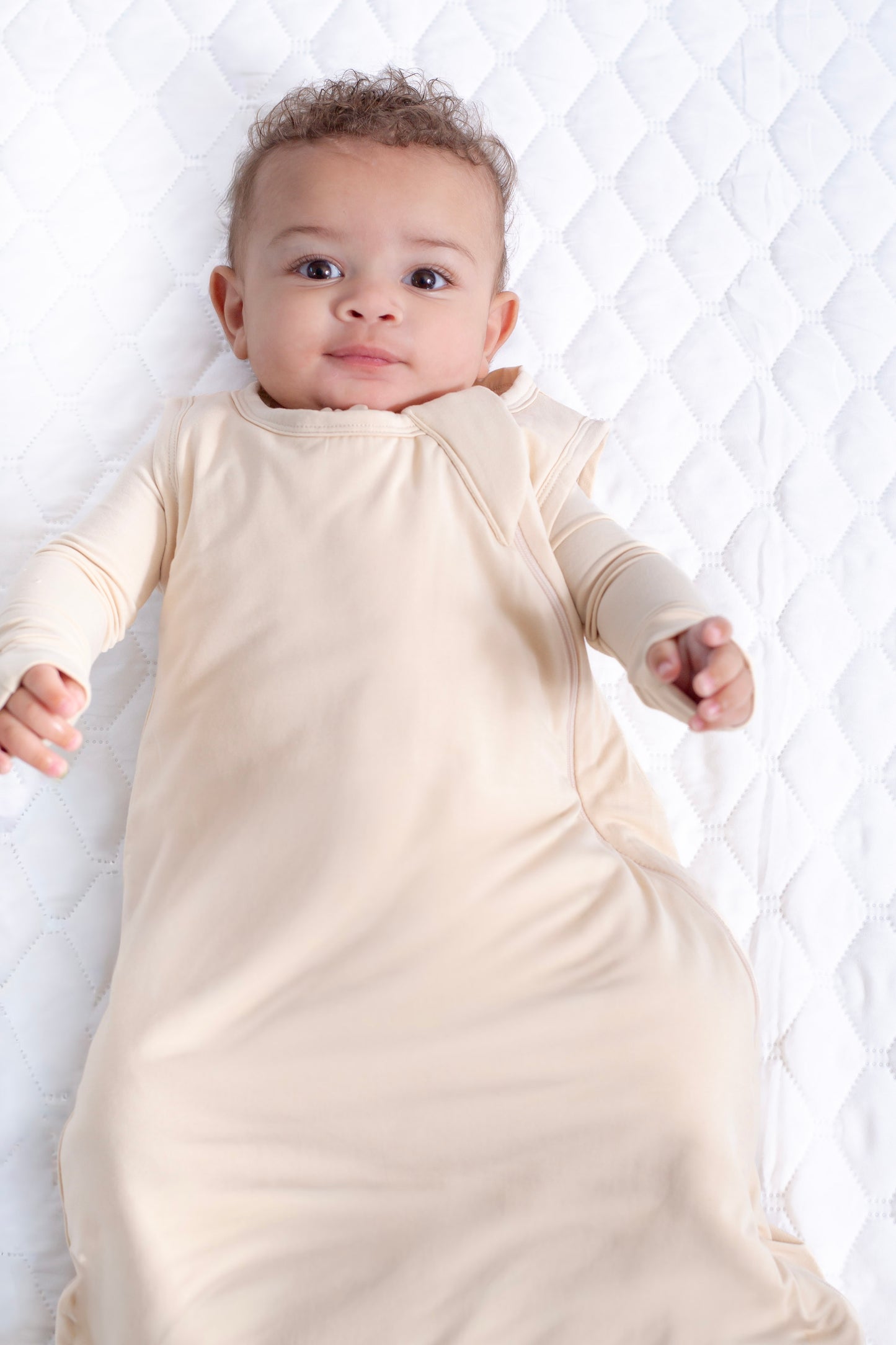 Baby wearing a beige onesie lying on a white textured surface