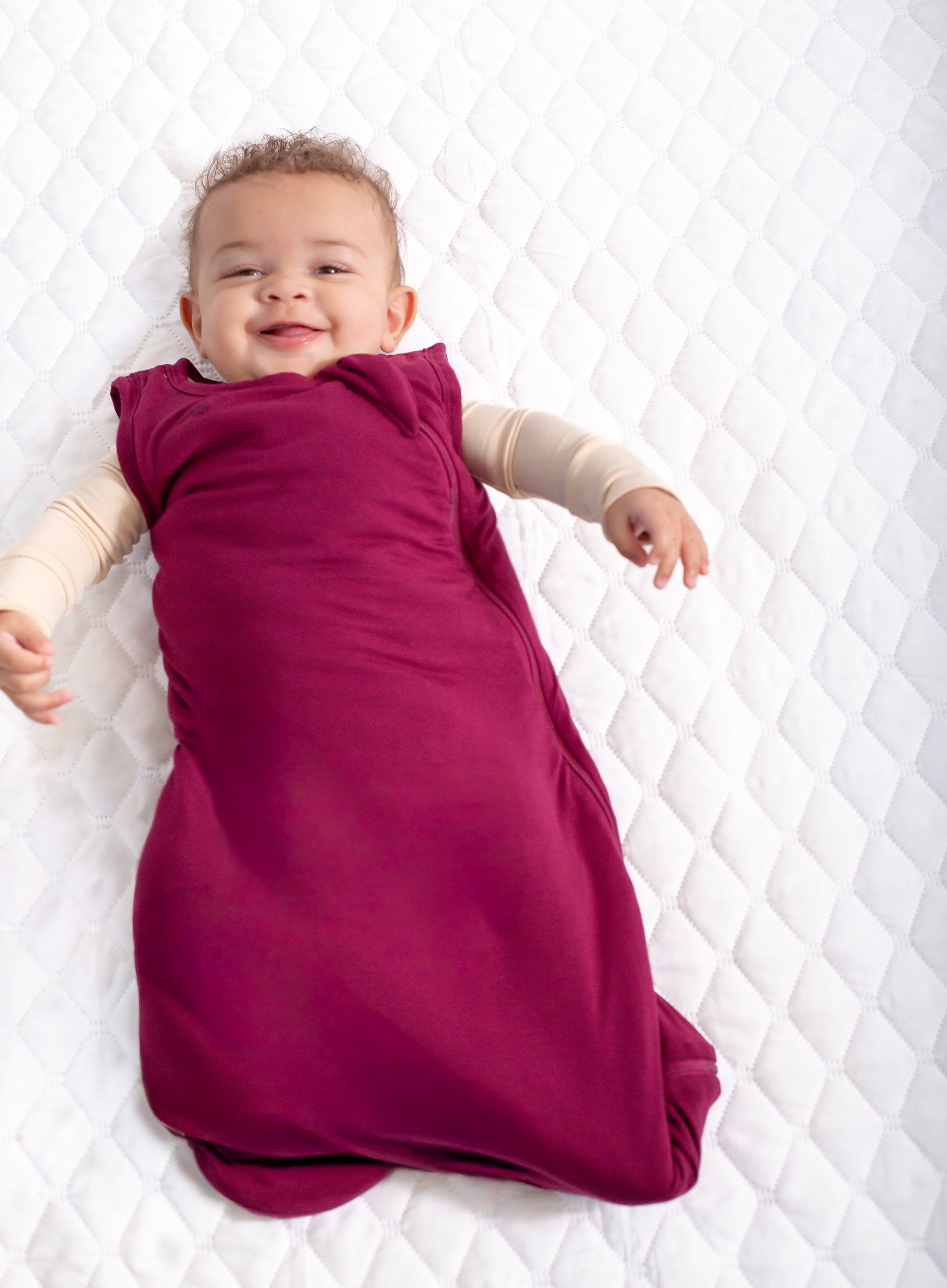 Baby lying on a white quilted surface wearing a purple sleep bag