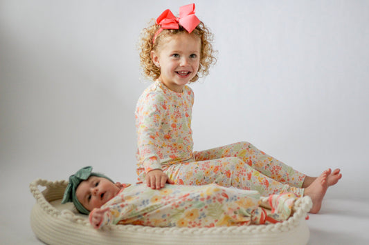 Two children in matching floral outfits sitting on a white background