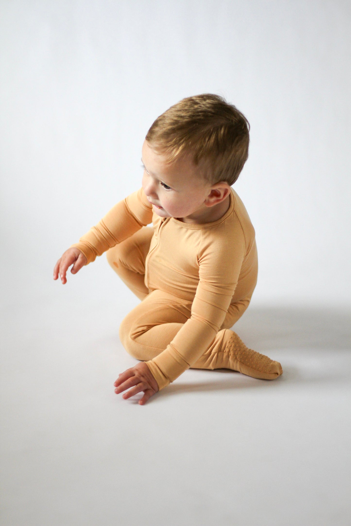 Child wearing a yellow onesie sitting on a white background
