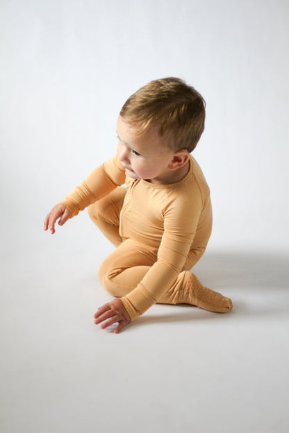 Child wearing a yellow onesie sitting on a white background