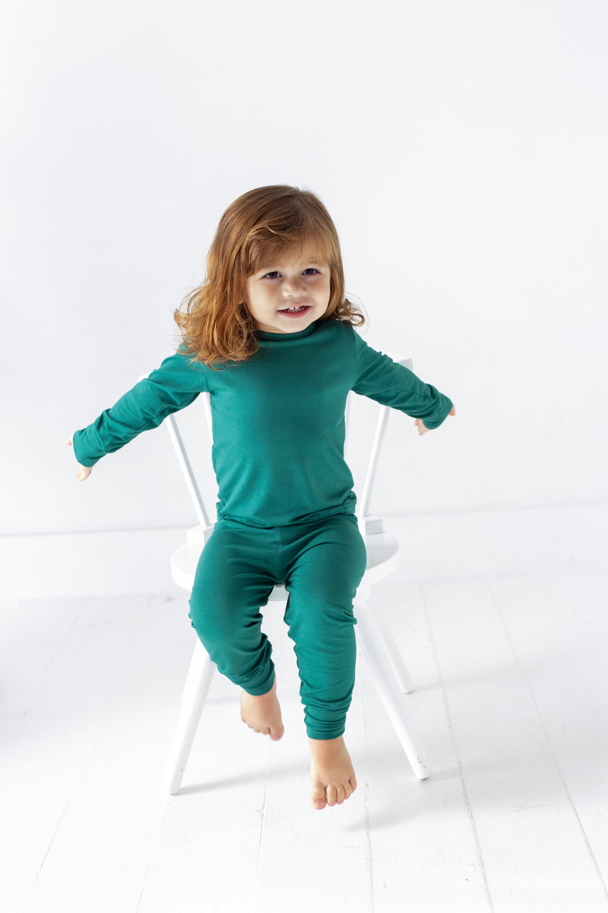 Child wearing a teal outfit sitting on a white chair against a light background