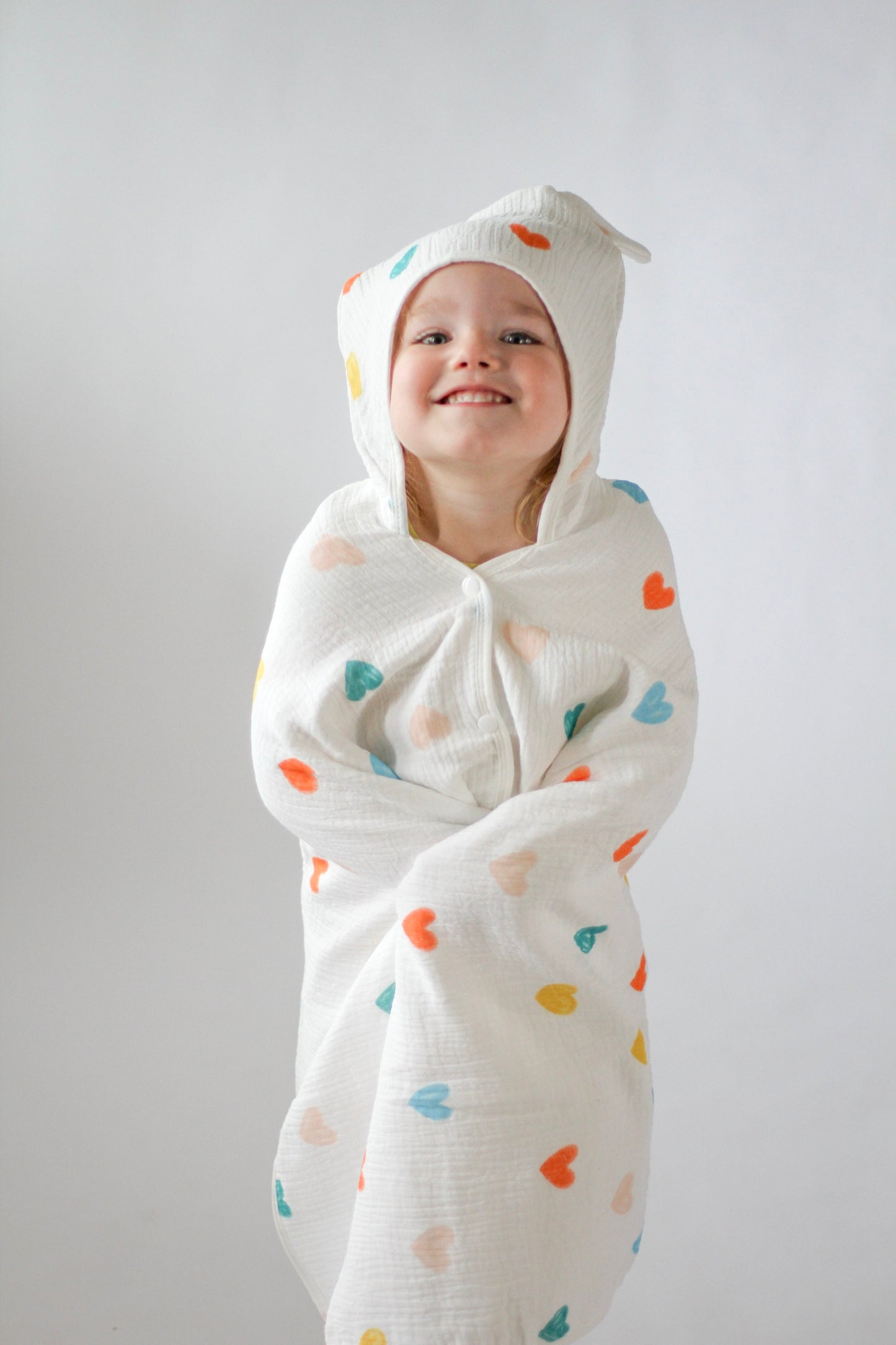 Child wrapped in a white swaddle with colorful heart patterns against a plain background