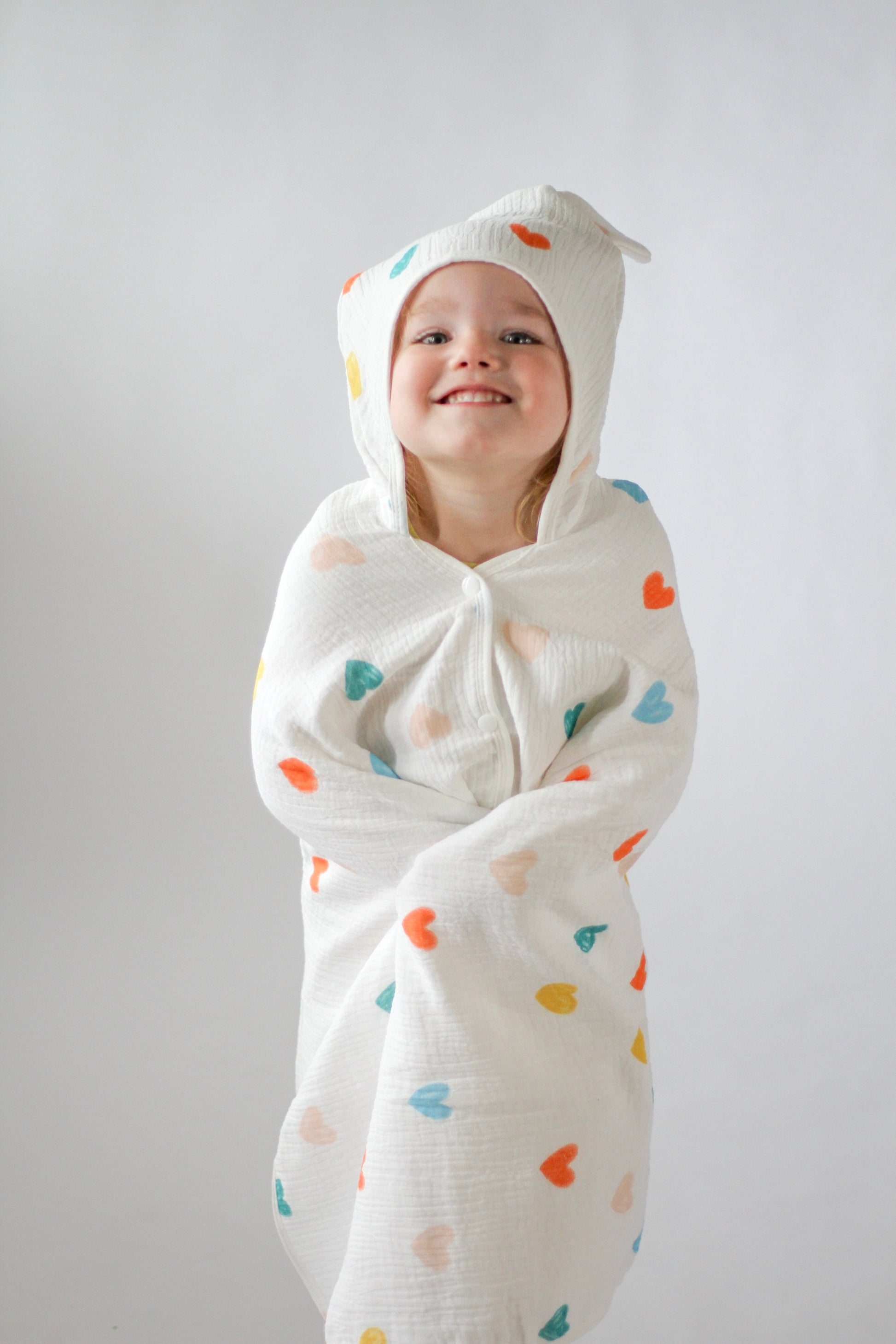 Child wrapped in a white swaddle with colorful heart patterns against a plain background