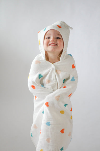 Child wrapped in a white swaddle with colorful heart patterns against a plain background