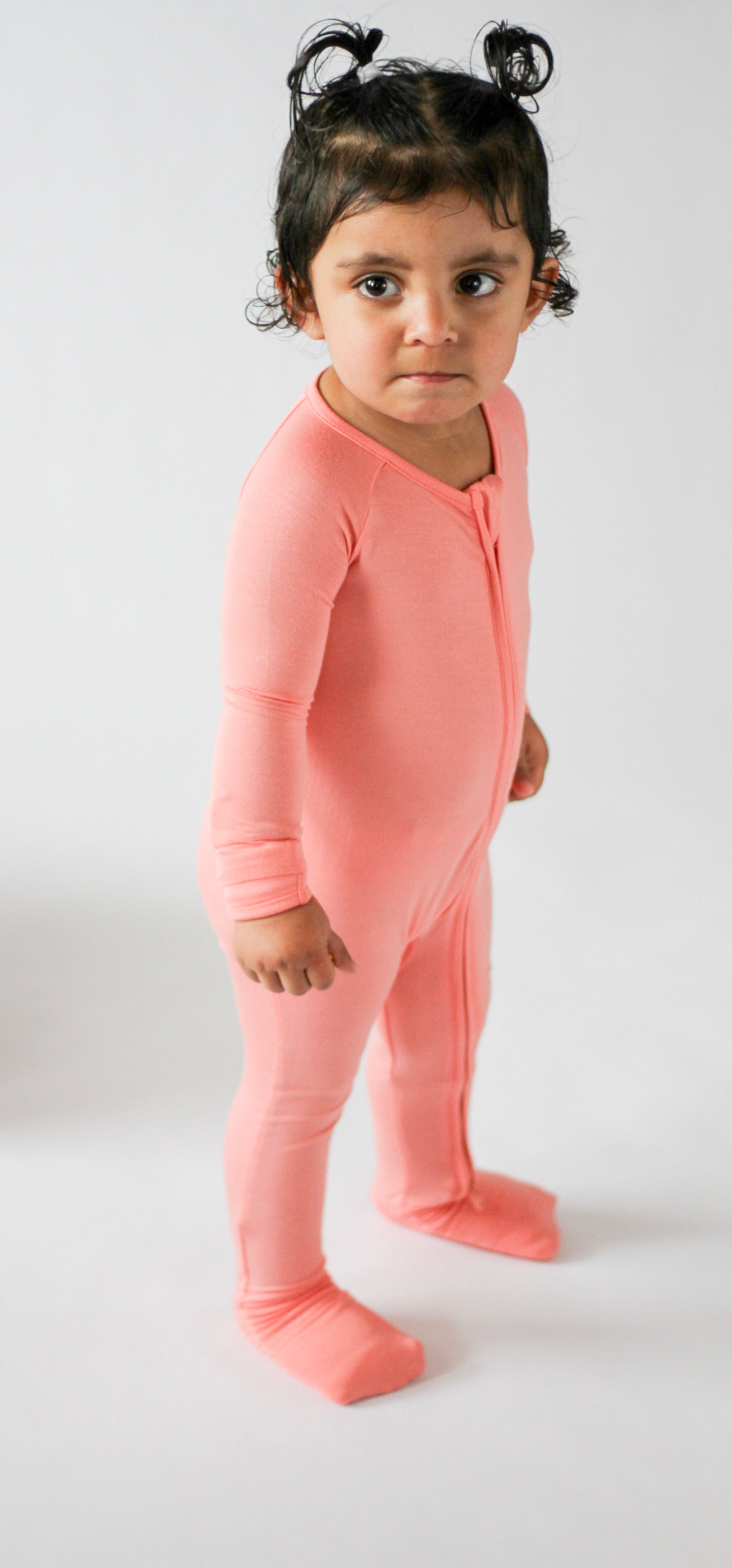 Child wearing a pink onesie against a white background