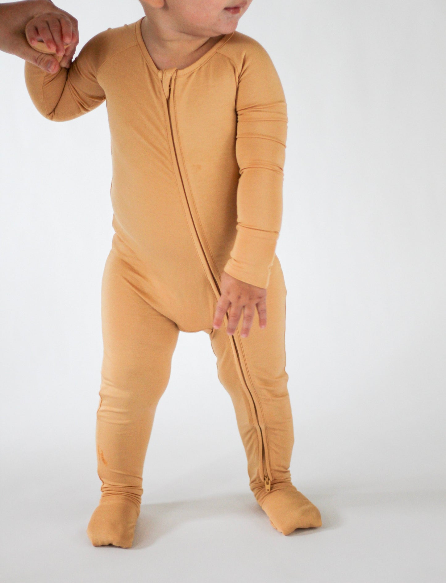 Child wearing a mustard yellow onesie on a white background