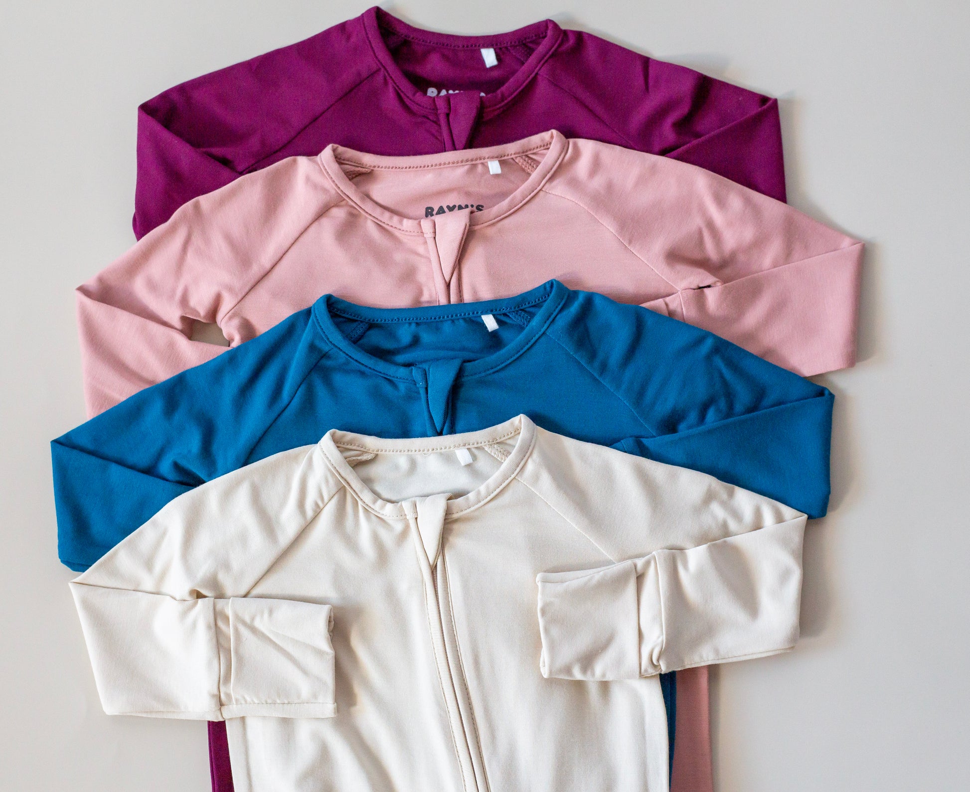 Four shirts in purple, pink, blue, and beige on a light gray background