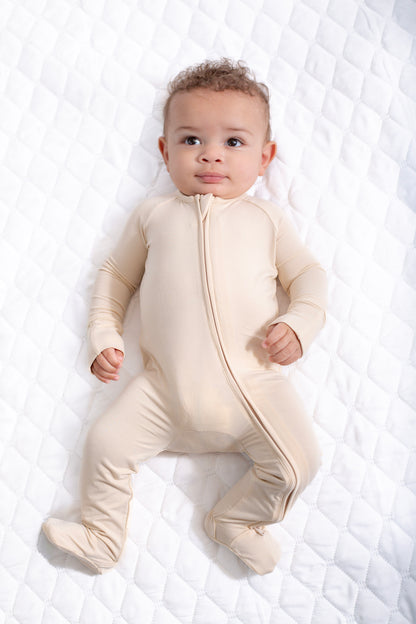 Baby wearing a beige onesie on a white textured surface