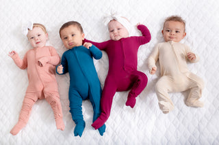 Four babies wearing colorful onesies on a white blanket