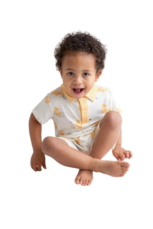 Child wearing a white outfit with yellow patterns sitting on a white floor.