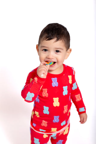 Child wearing a red pajama set with teddy bear patterns, holding a colorful object.