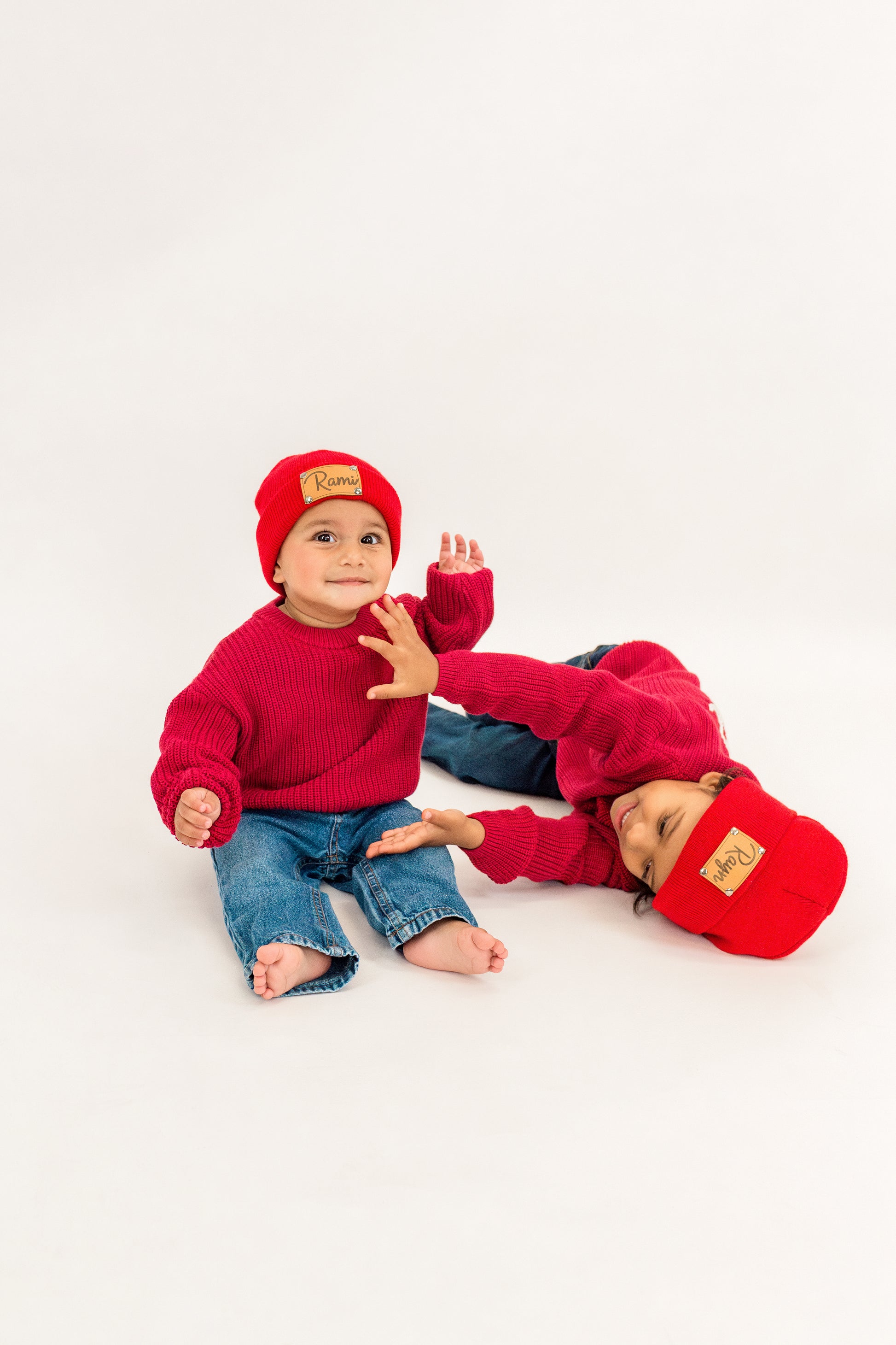 Two children wearing red outfits with beanies on a white background