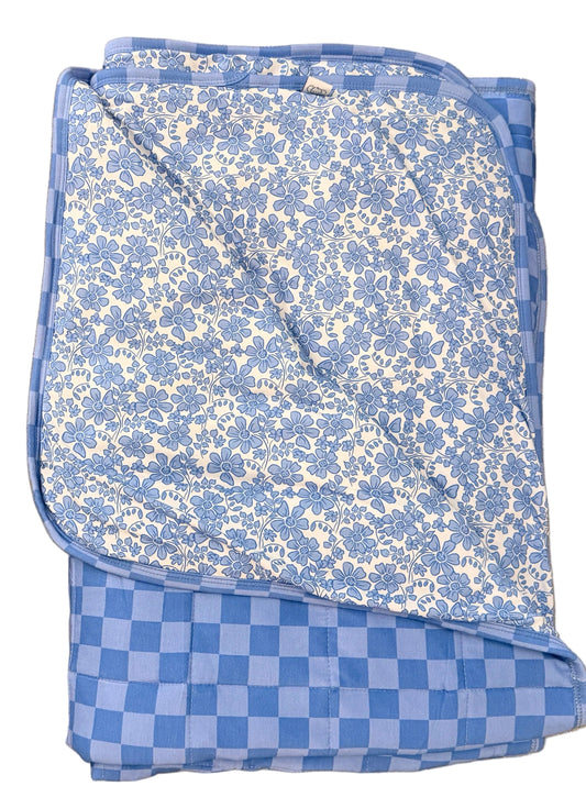 Folded blue floral blanket on a beige floor with gold sandals nearby