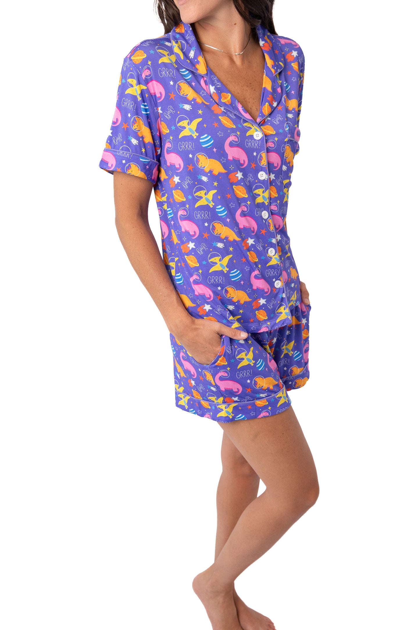 A woman modeling a matching short-sleeve pajama top and shorts set with a colorful mermaid print on a purple background, shown against a plain white studio background.