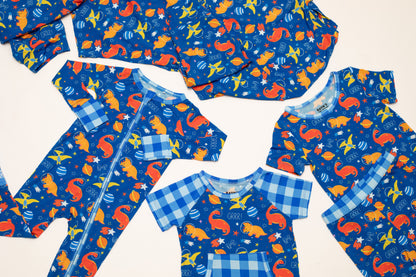 A coordinated baby clothing set laid flat on a light background, including a long-sleeve zip bodysuit and several short-sleeve tops. The fabric has a blue base with a playful print of orange squirrels, yellow birds, blue fish, and white stars, plus light blue gingham trim.